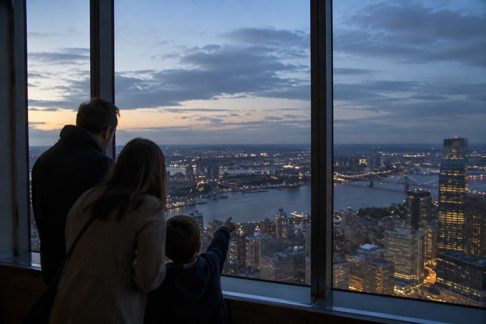 A family pointing at landmarks through a tall observation deck window