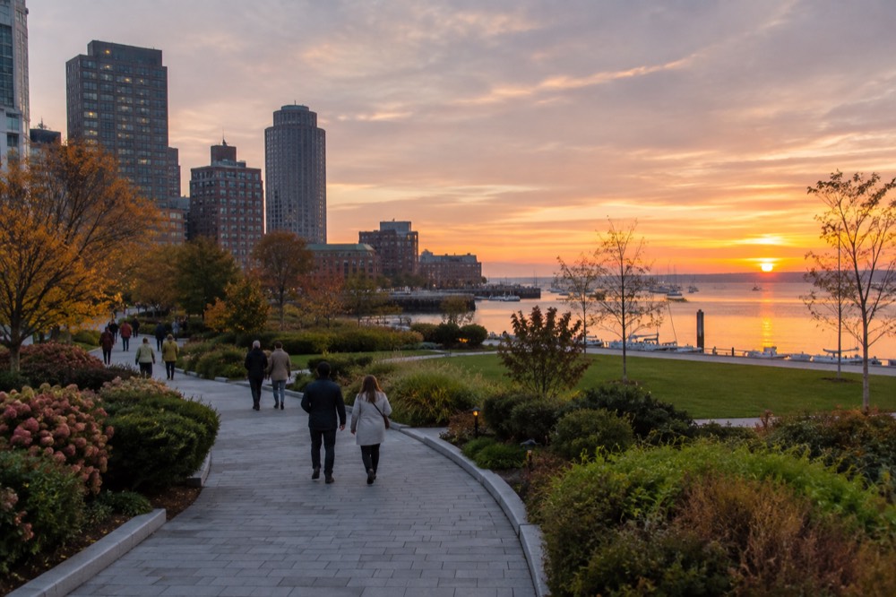 People strolling a landscaped park corridor with gardens on both sides at golden hour