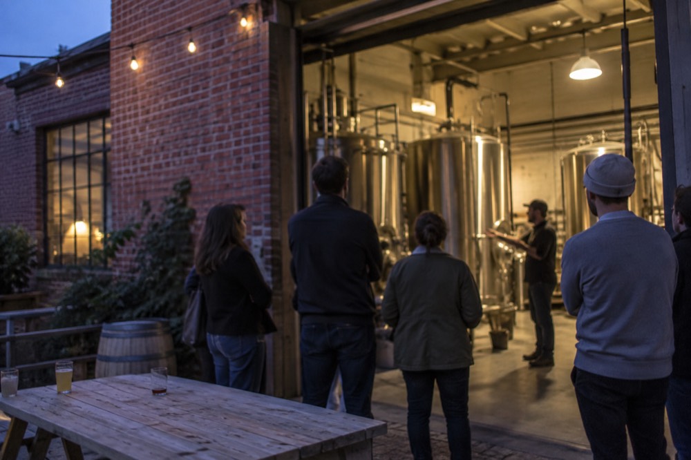 A guide explaining brewing equipment to a small group inside a brewery