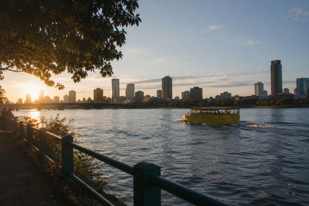 An amphibious tour vehicle cruising on the Charles River with the Boston skyline behind it