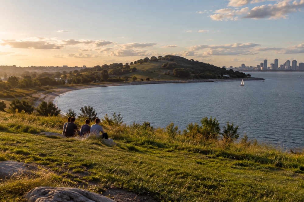 A green island with a hill rising over a beach, seen across the water from Boston Harbor
