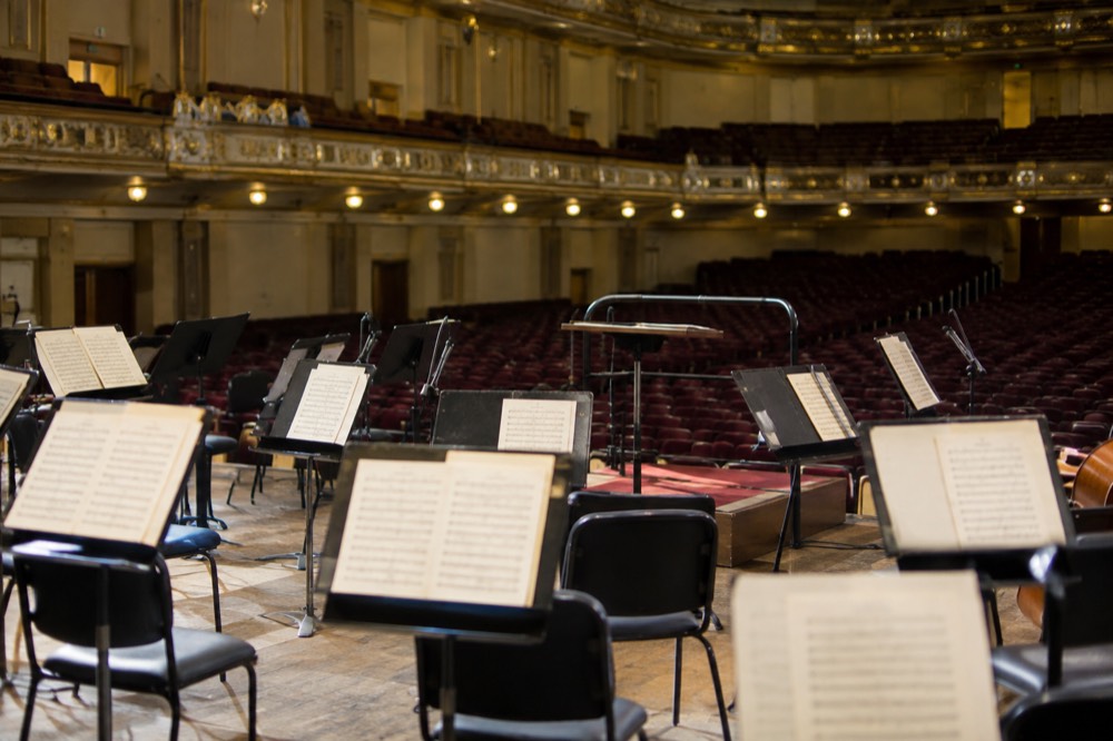 A conductor's podium and music stands under stage lights before an empty auditorium
