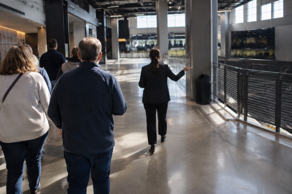 A guide leading a small group of visitors through an arena concourse on a tour