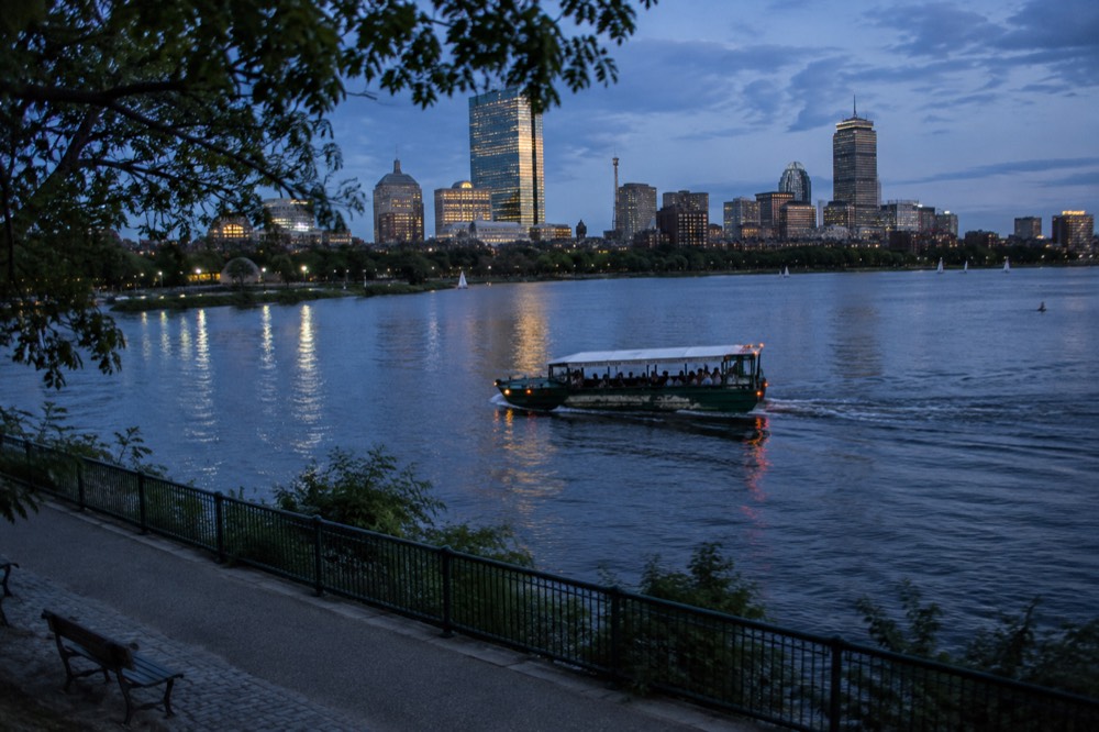 An amphibious duck boat riding on the Charles River with the Boston skyline behind it