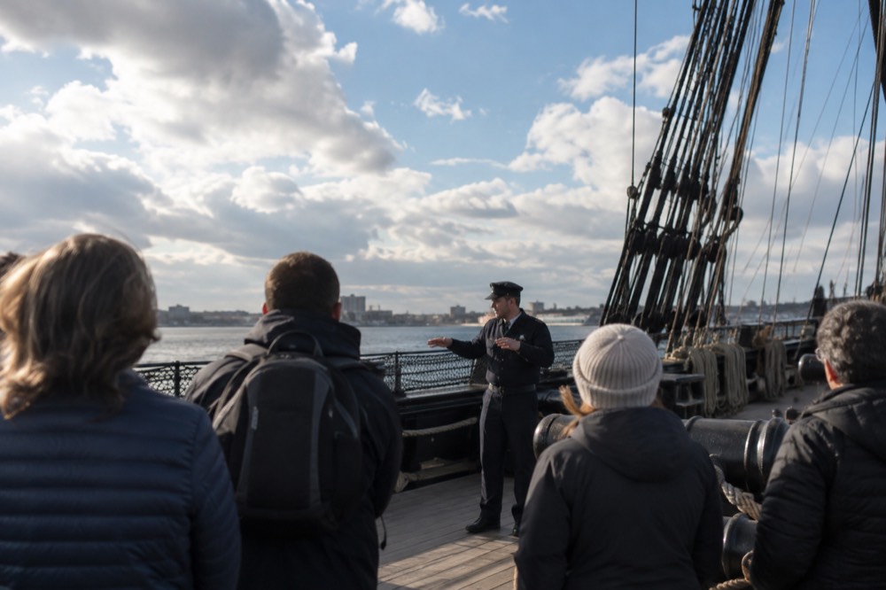 A uniformed sailor describing the ship's deck to a small group of visitors