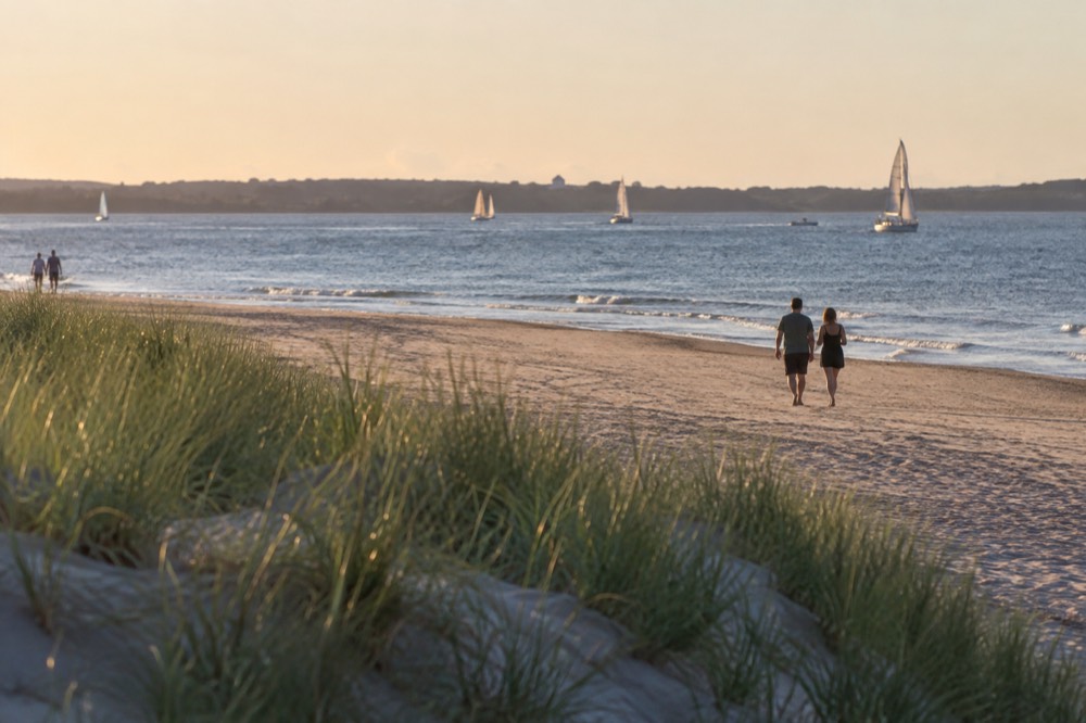 A wide sandy beach with calm water and a view of sailboats near Boston
