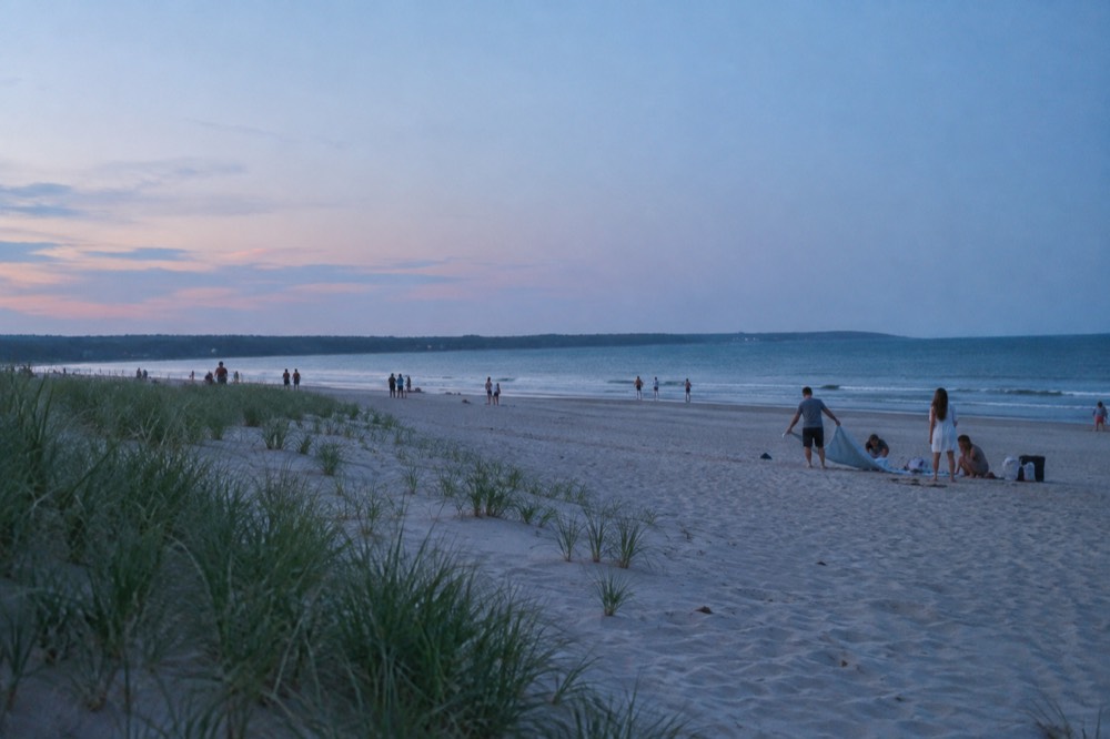 Families spreading towels on a wide public beach near Boston on a summer afternoon