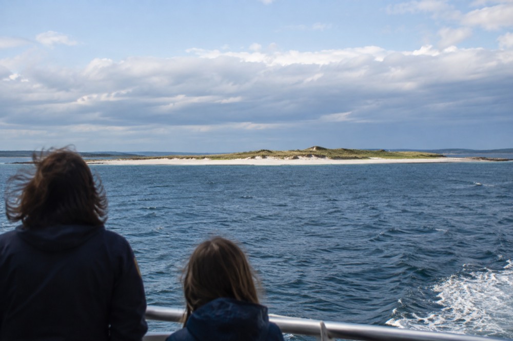 A ferry crossing open water toward an island with low dunes and beach grass