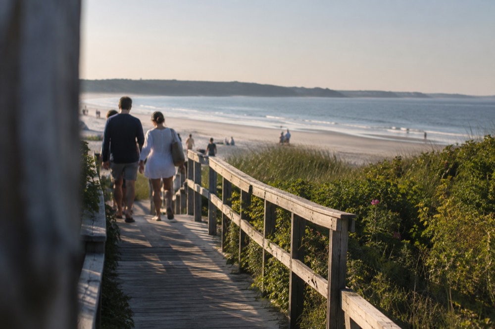 People walking along a beach boardwalk in warm summer light