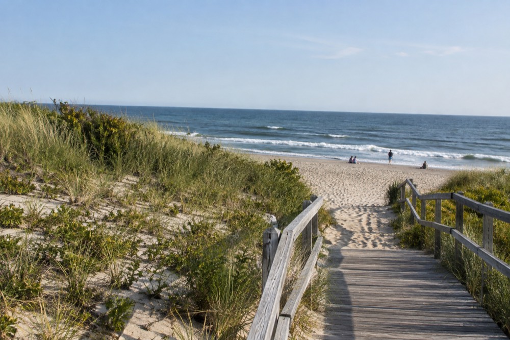 Sandy Cape Cod beach with grassy dunes and a wooden walkway leading toward the water