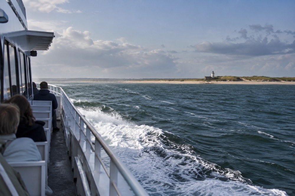 A high-speed passenger ferry crossing open water toward a sandy point of land