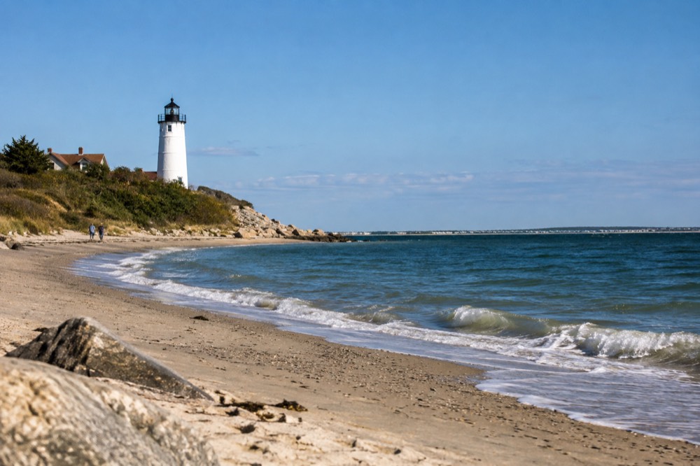 A white lighthouse standing above a curved sandy beach under a clear sky