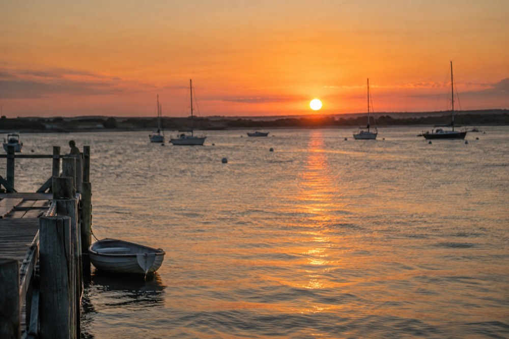 Sunset over a calm Cape Cod harbor with sailboats at anchor and a orange sky
