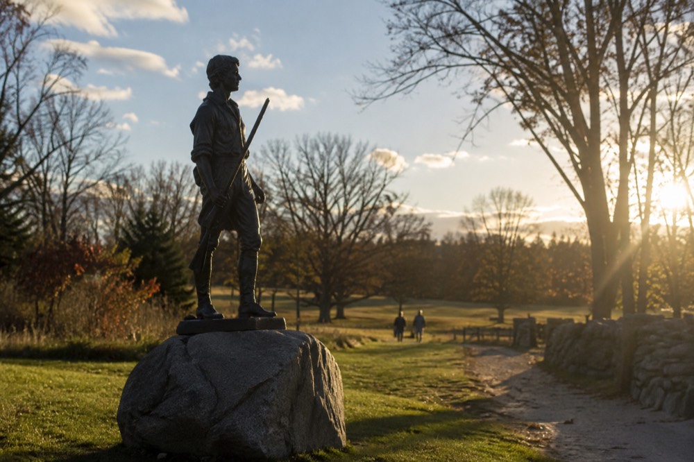 The Minute Man statue standing on a grassy field beside a historic stone path