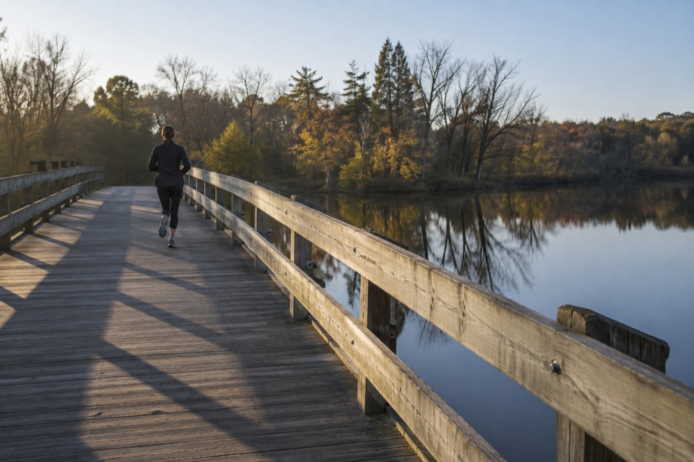 A wooden bridge over a slow river with trees reflected in the water