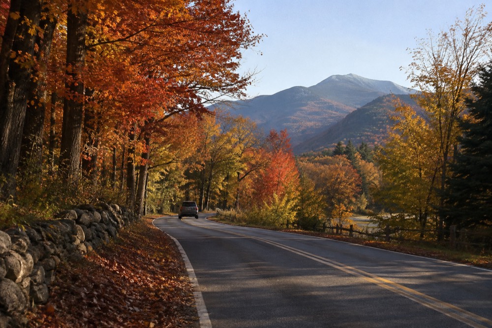 A country road in New England lined with red and orange maple trees in autumn