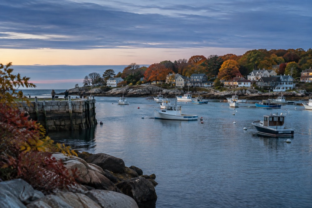 A granite harbor in Rockport with autumn trees along the shoreline