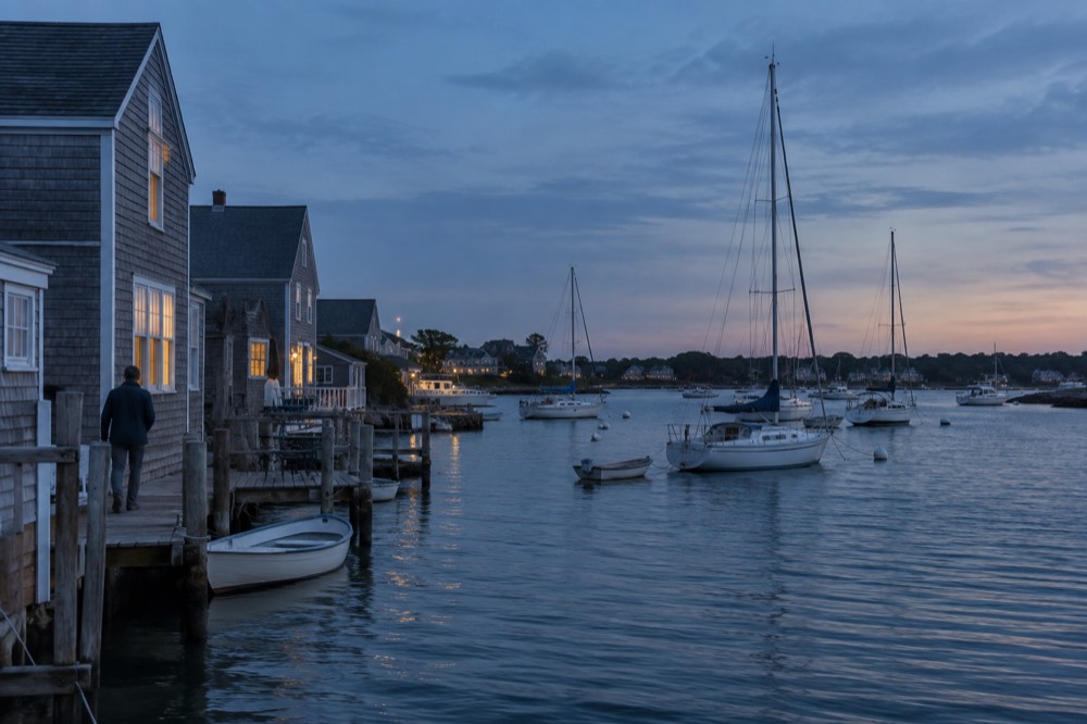 Sailboats moored in a small harbor with weathered shingled buildings along the shore