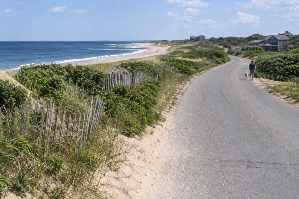 A coastal road curving past dunes and beach grass toward the horizon