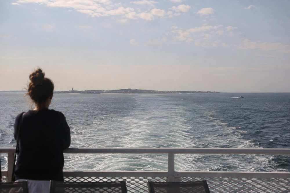 A ferry wake cutting across calm gray-blue ocean water with a distant island shoreline