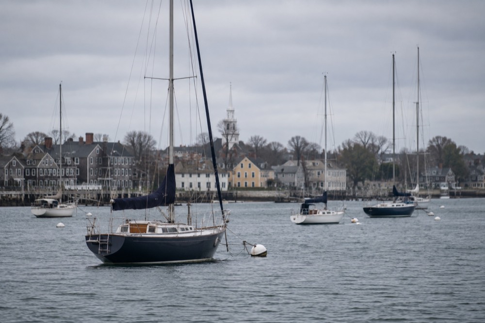 Sailboats anchored in Newport Harbor with colonial-era buildings along the waterfront