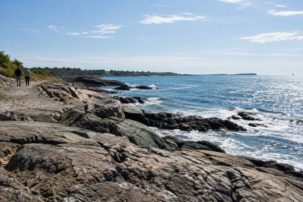 A quiet rocky shoreline path with waves and open water beyond