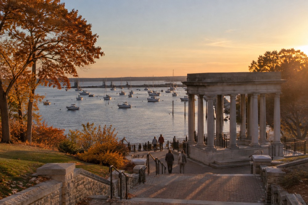 A harbor waterfront with a granite memorial canopy and boats at mooring in autumn light