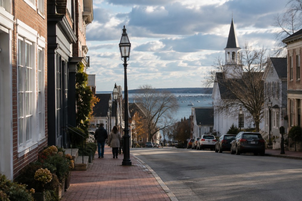 A small coastal town main street with brick storefronts and a church spire