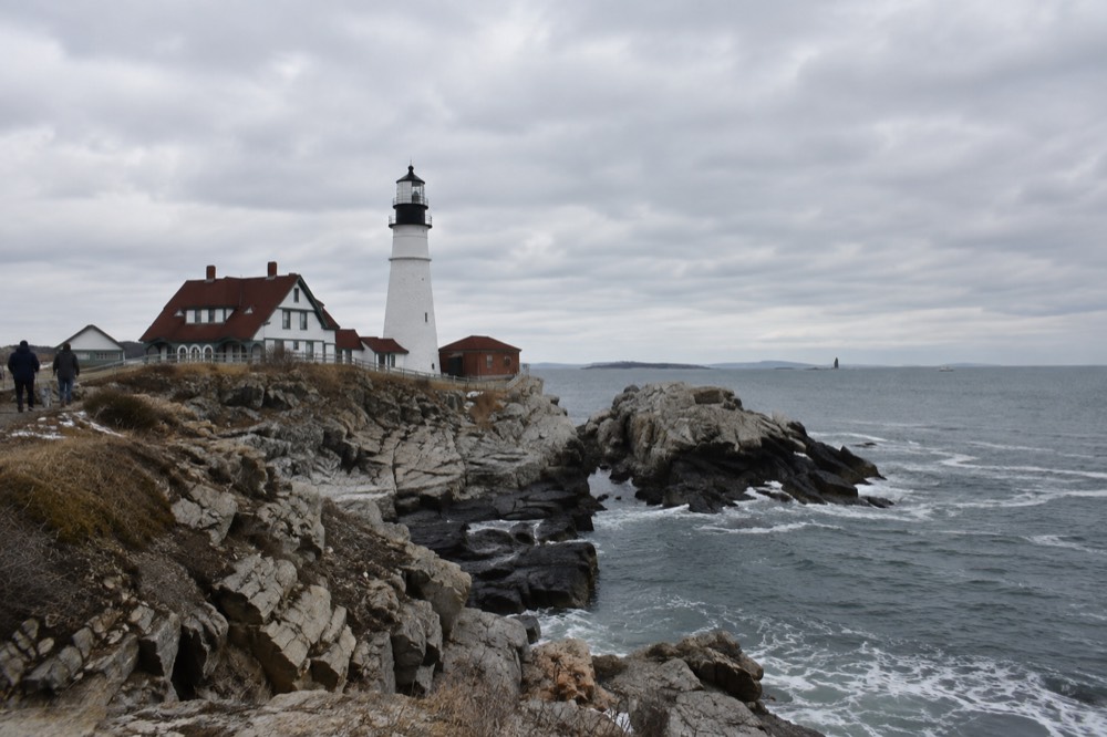 A white lighthouse on a rocky headland overlooking Casco Bay