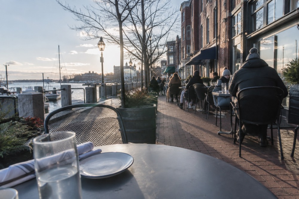 Diners at outdoor tables along a brick sidewalk restaurant row