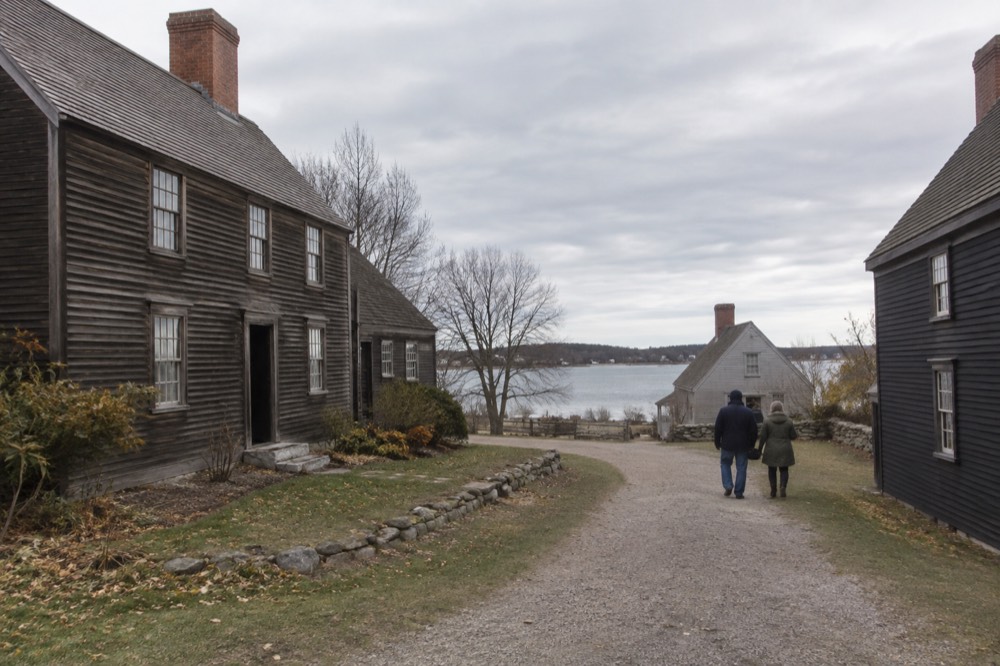 Visitors walking a gravel path between historic wooden houses at an outdoor history museum