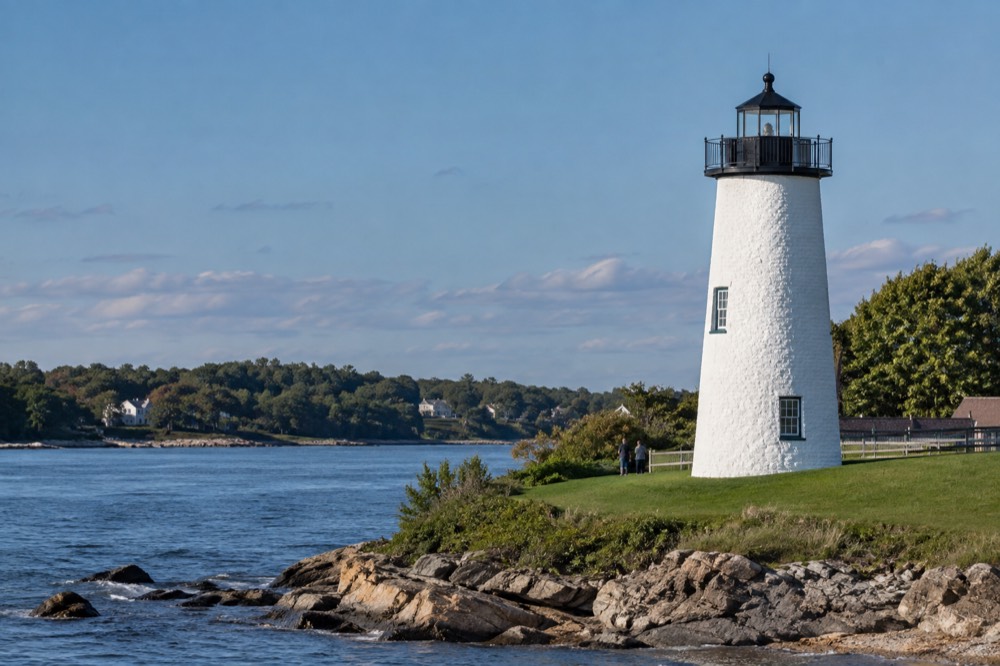 A white lighthouse standing on a green lawn beside a river mouth