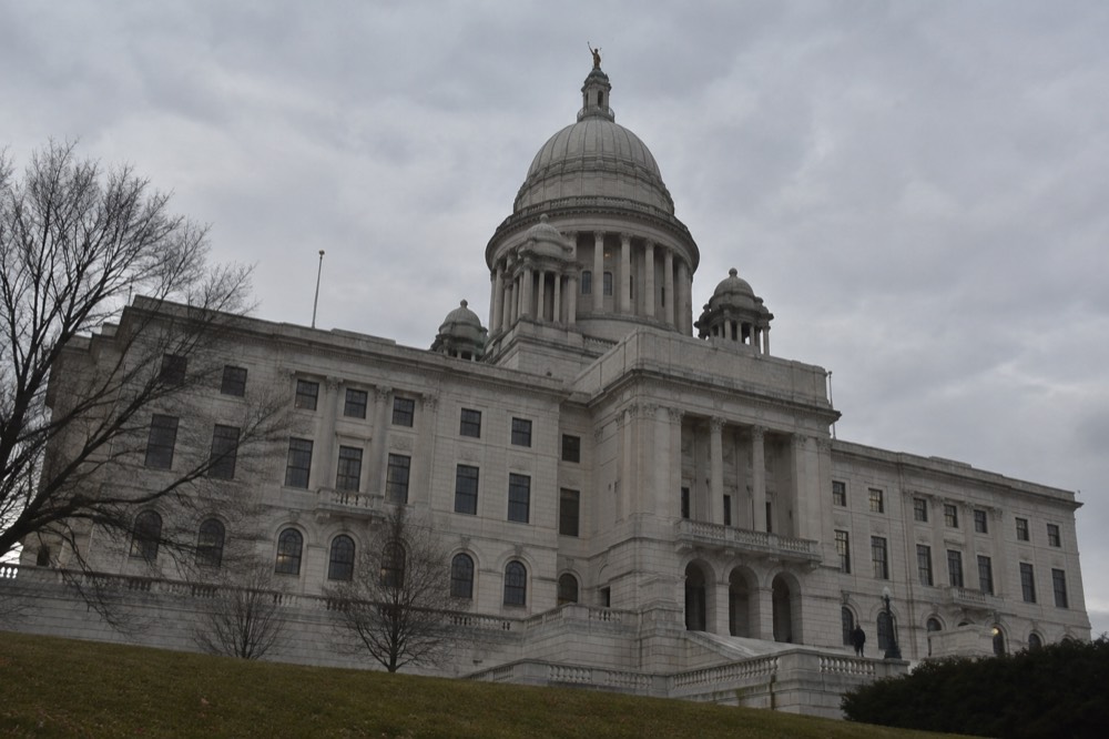 A marble state capitol building with a large dome under a cloudy sky