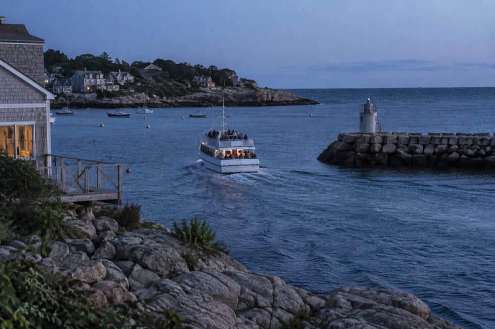 A whale watching boat heading out of a harbor past a breakwater on a clear morning