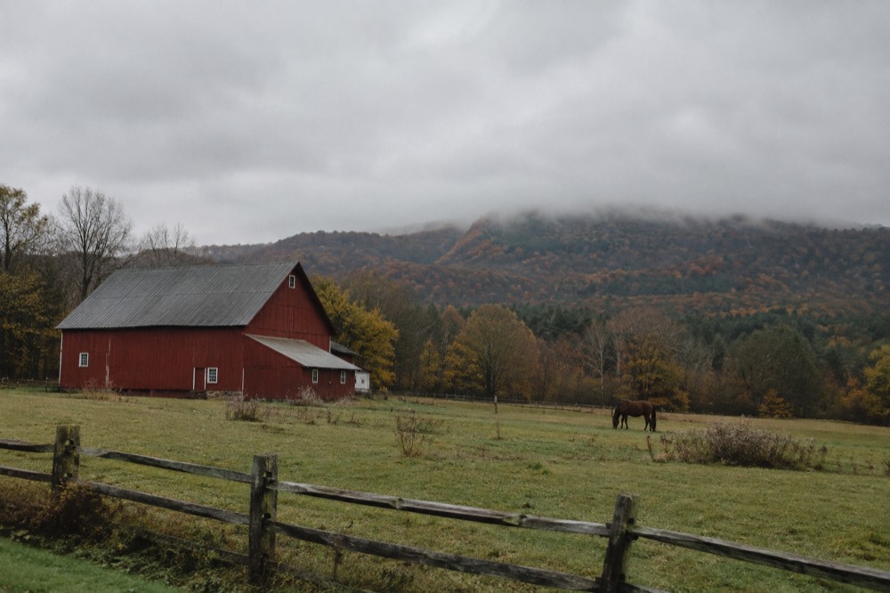 A red barn and pasture with forested hills rising behind it