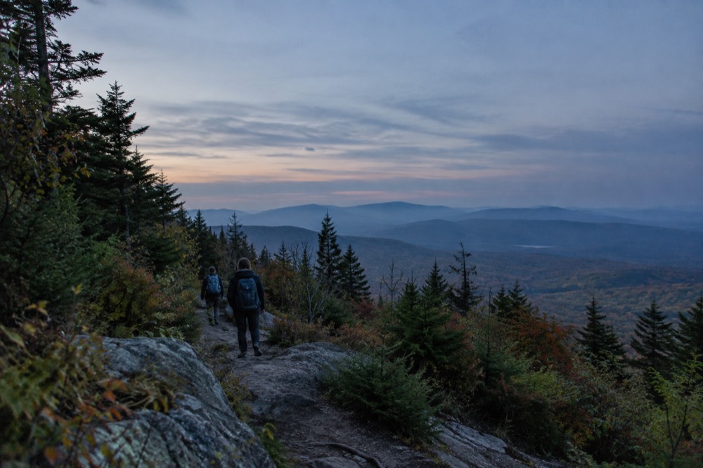 Hikers on a wooded ridge trail with hazy mountains in the distance