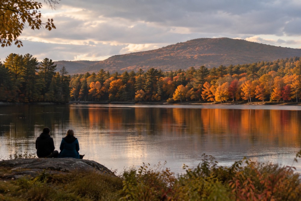 A lake reflecting orange autumn trees with hills behind it at golden hour
