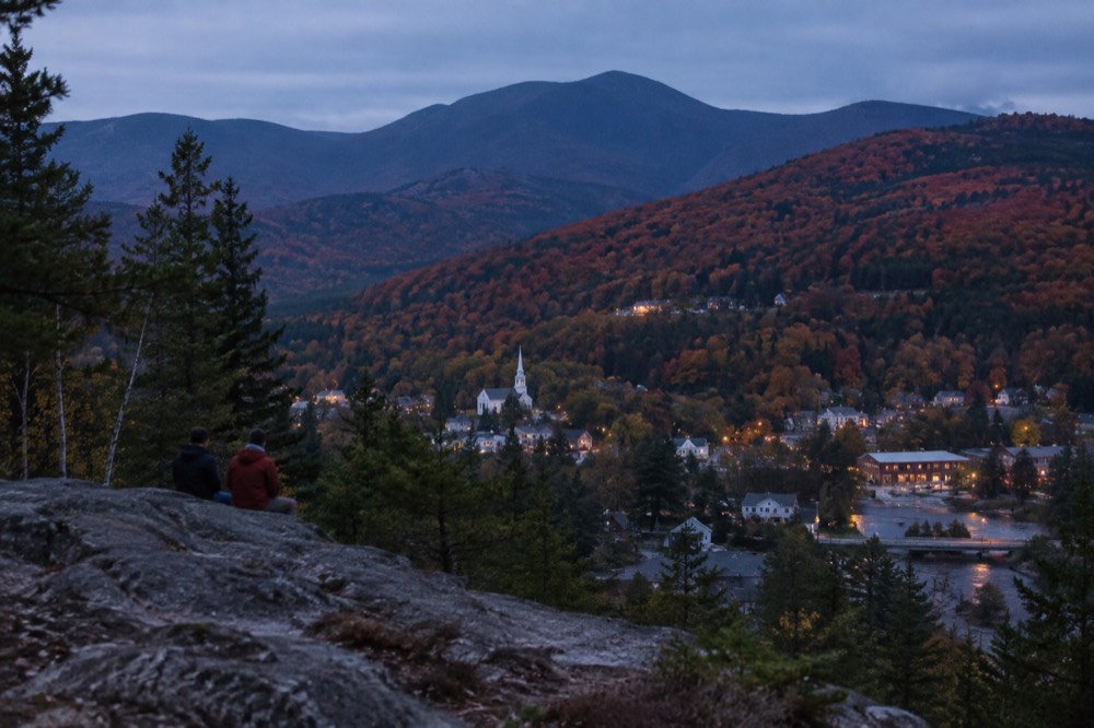 Hillsides covered in red and orange autumn trees above a valley town
