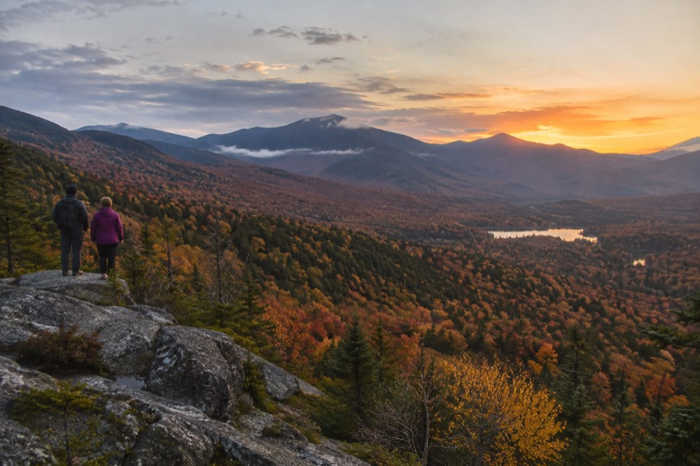 A valley of autumn trees with distant mountain peaks at sunset