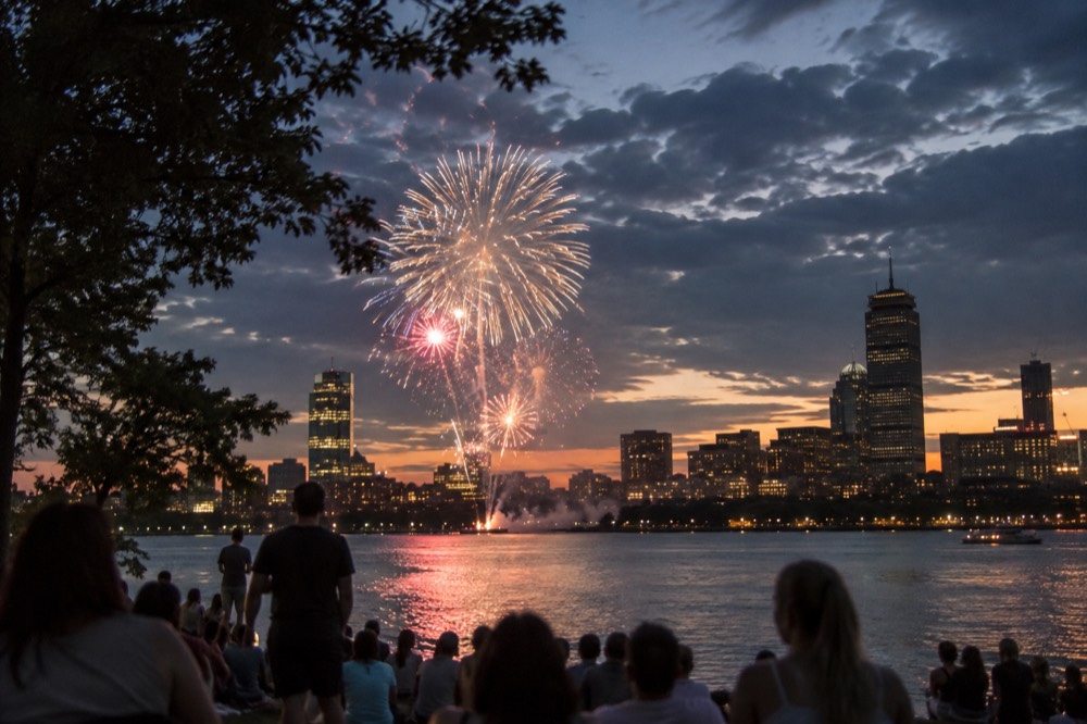 Fireworks bursting over the Charles River with the Boston skyline lit behind them
