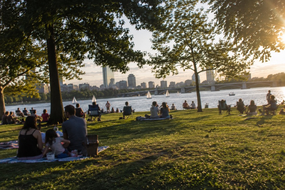 Families with blankets and chairs on the grass of the Charles River Esplanade during a summer afternoon