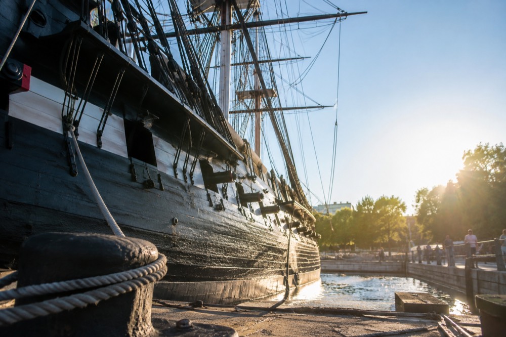 The wooden hull of USS Constitution docked at the Charlestown Navy Yard under a clear sky