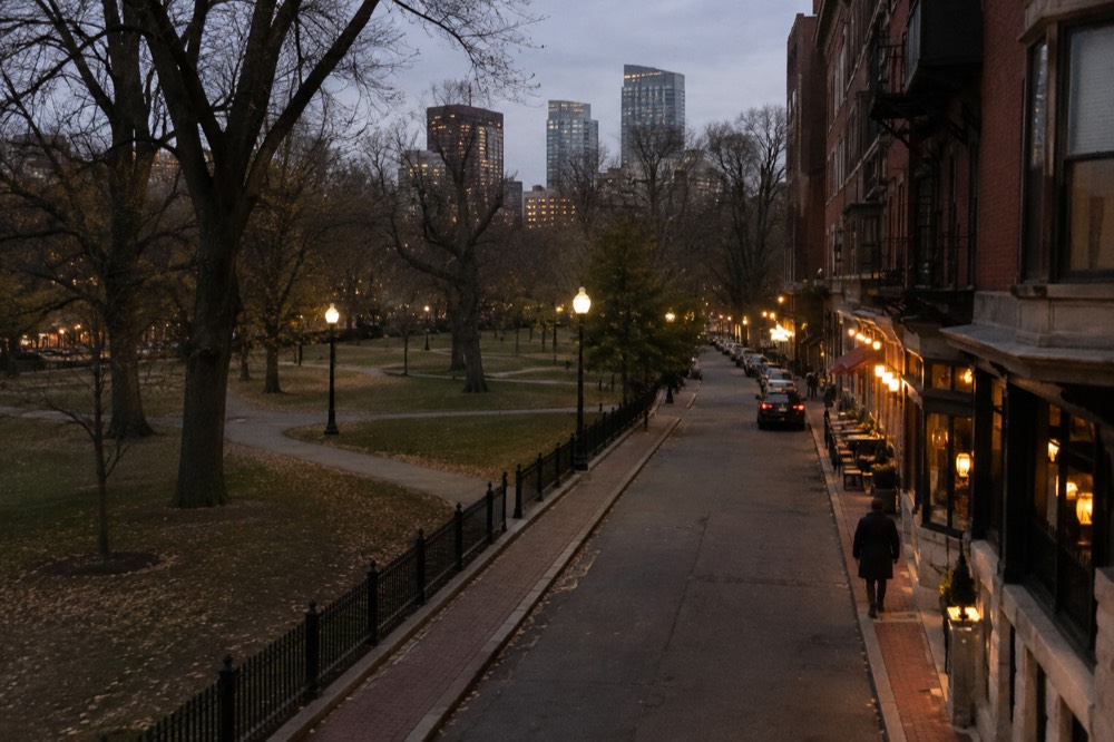 A narrow Boston street at dusk with warm light spilling from restaurant windows