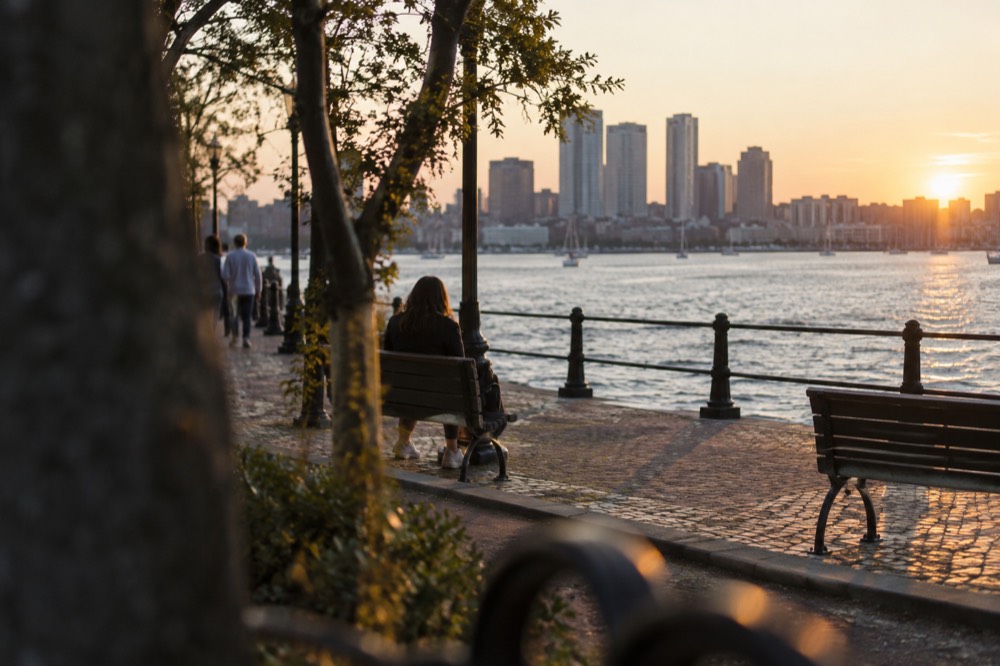 A level brick waterfront path along Boston Harbor with benches and railing