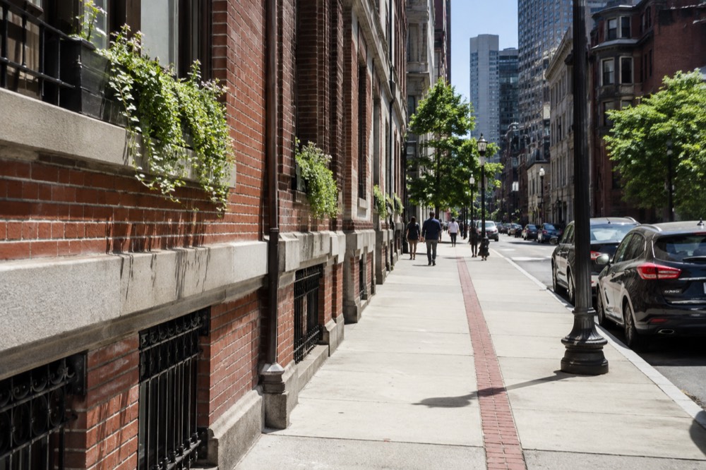 A red brick line running along a flat downtown sidewalk past historic buildings