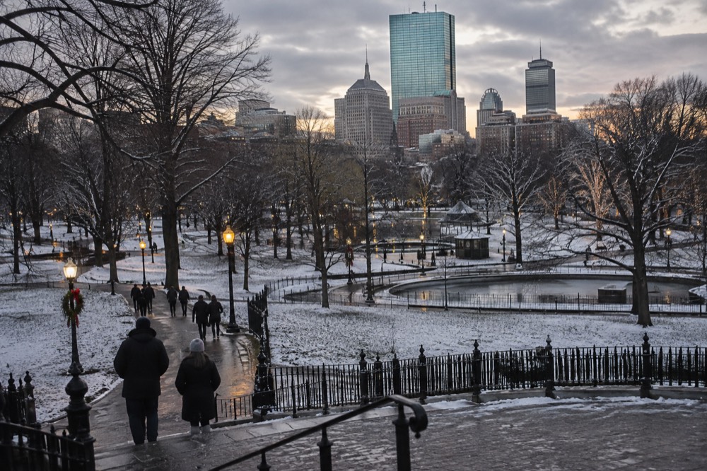 A snow-dusted Boston Common with holiday lights and the skyline beyond