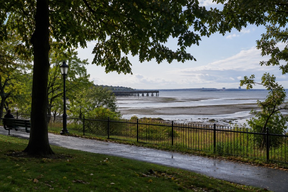 A wide tidal flat at low tide with exposed wet sand, shallow pools and a distant pier