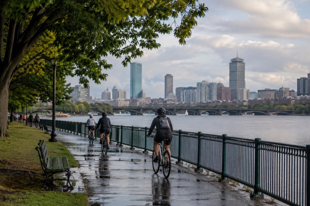 Cyclists riding along a riverside path with a city skyline across the water