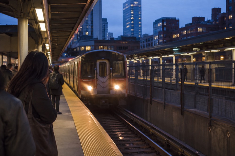 A subway station platform with a train arriving and riders waiting