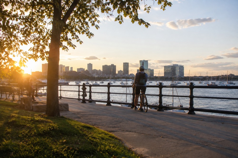 A cyclist pausing at a railing overlooking a harbor at golden hour